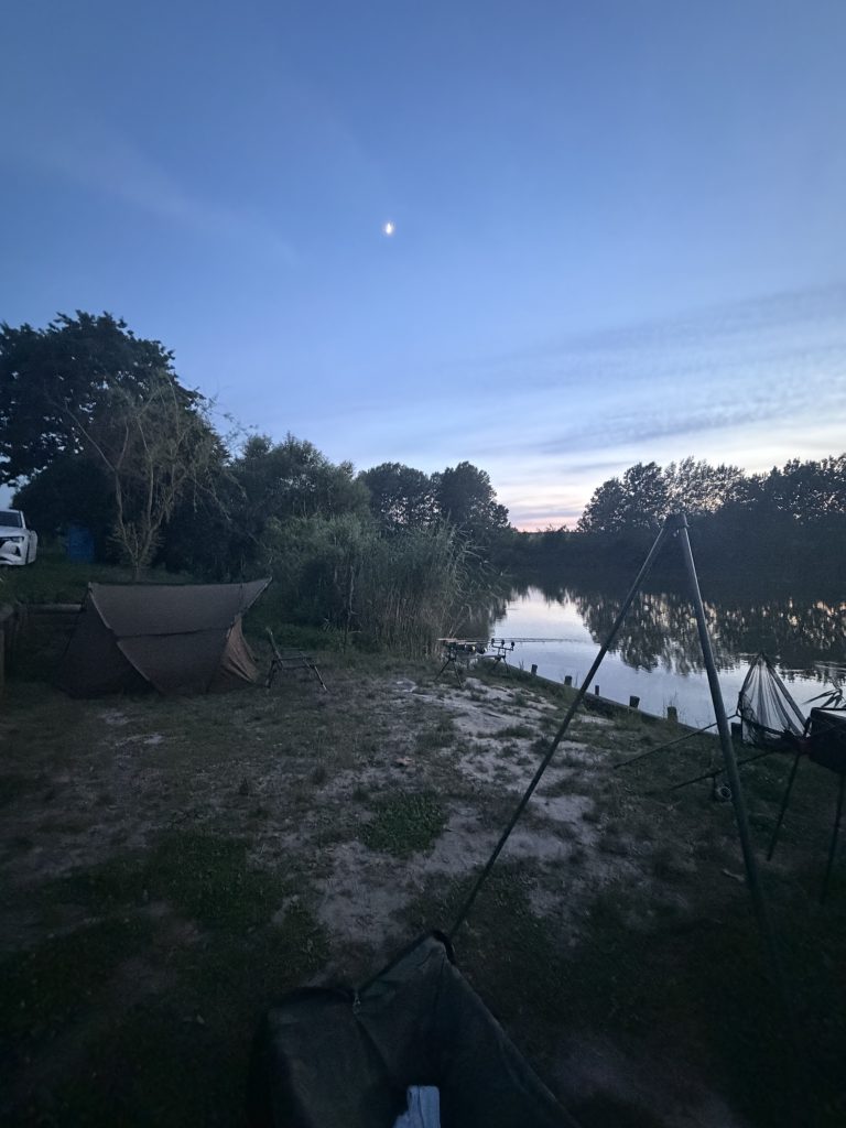 Night carp fishing setup with rods and shelter beside the lake
