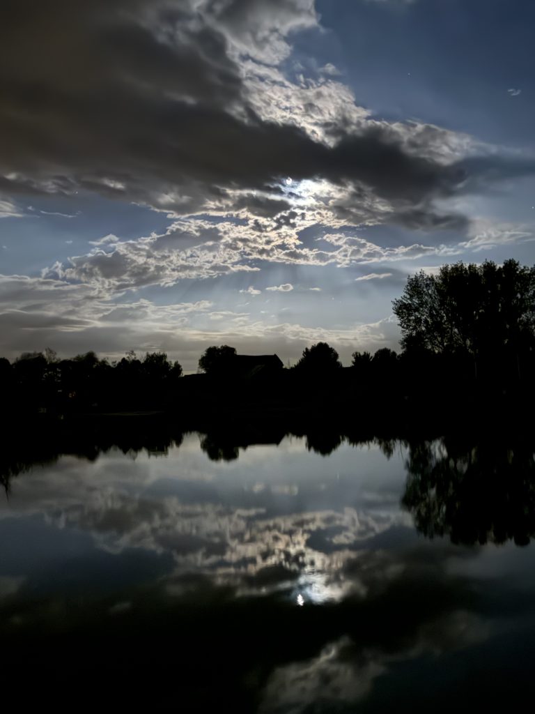 Full moon shining through clouds above a calm freshwater lake at night