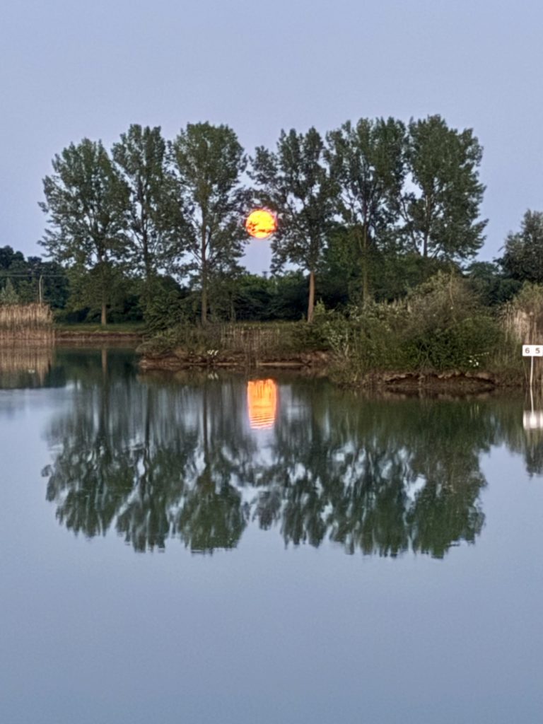 Full moon rising over a calm freshwater lake with trees reflected in the water