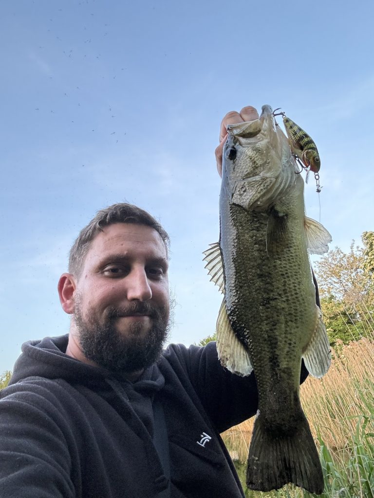 Angler holding a largemouth bass caught on a hard fishing lure near shoreline vegetation